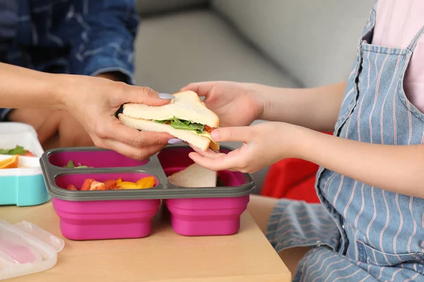 Mother packing school lunch for her little daughter at home