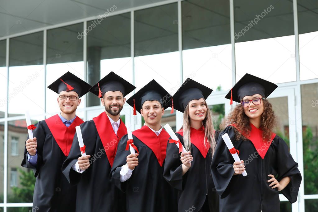 Happy students in bachelor robes and with diplomas outdoors