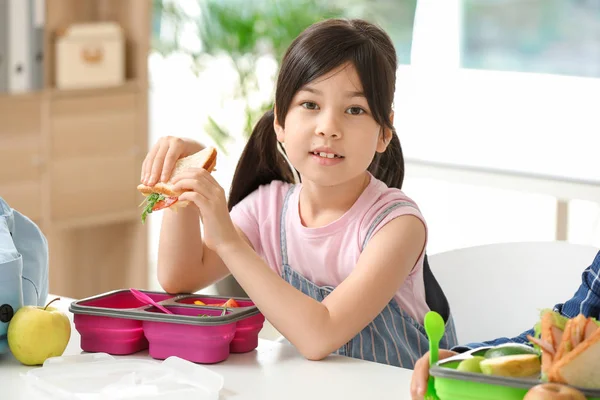 Little schoolgirl eating tasty lunch in classroom — Stock Photo, Image