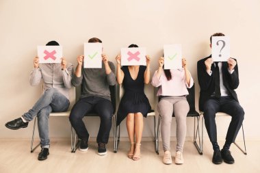 Gençler kapalı koltuklarda otururken farklı işaretler ile kağıt levhalar tutan genç insanlar. İş görüşmesi kavramı