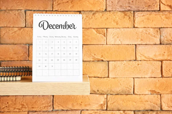 Shelf with flip paper calendar on brick wall — Stock Photo, Image