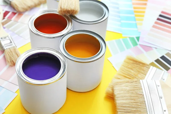 Cans of paints with brushes and palette samples on color background