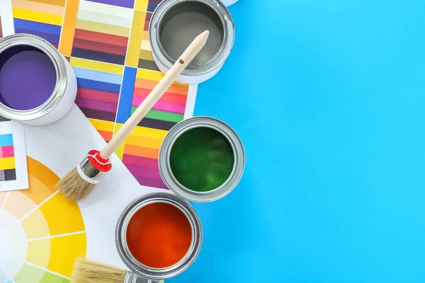 Cans of paints with brushes and palette samples on color background