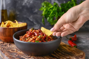Woman eating tasty chili con carne with nachos clipart