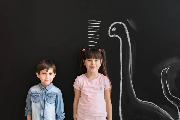 Cute little children measuring height near wall with marks and drawn dinosaur — Stock Photo, Image