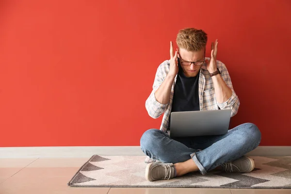 Stressed young man with laptop sitting near color wall — Stock Photo, Image