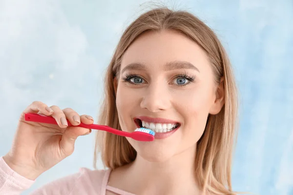 Beautiful woman cleaning teeth on light background