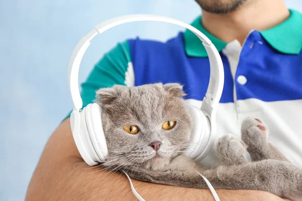 Young man and his cute funny cat with headphones on color background — Stock Photo, Image