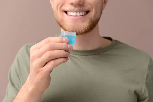 Молодой человек с чашкой жидкости для полоскания рта на цветном фоне — стоковое фото