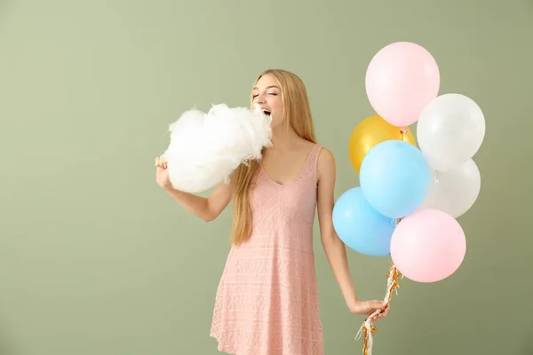 Schöne Frau mit Zuckerwatte und Luftballons auf farbigem Hintergrund — Stockfoto