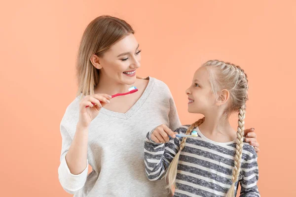 Little girl and her mother cleaning teeth on color background — Stock Photo, Image