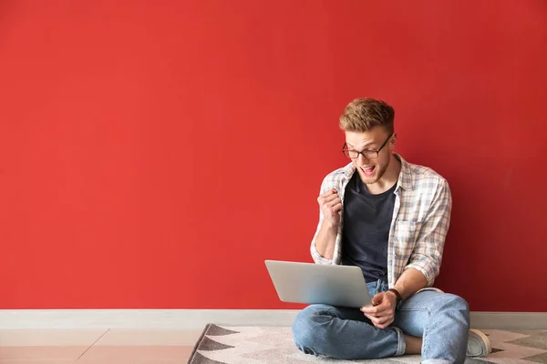 Happy young man with laptop sitting near color wall — Stock Photo, Image