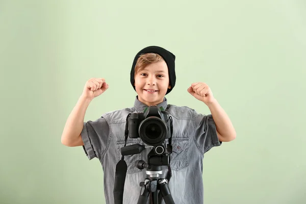 Cute little photographer with professional camera on color background — Stock Photo, Image