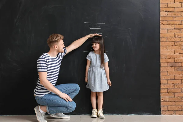 Father measuring height of his little daughter near wall with marks — Stock Photo, Image