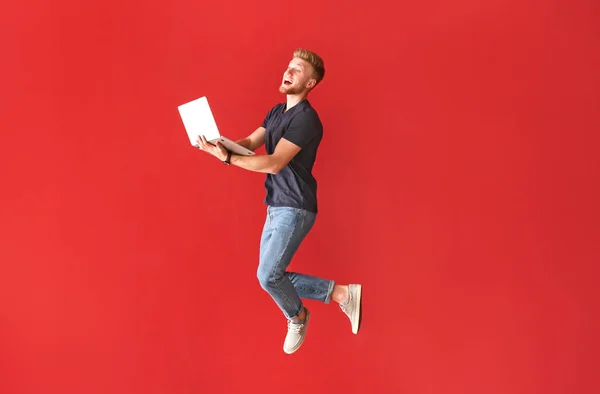 Jumping young man with laptop on color background — Stock Photo, Image