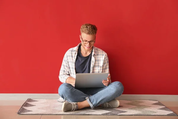 Handsome young man with laptop sitting near color wall — Stock Photo, Image