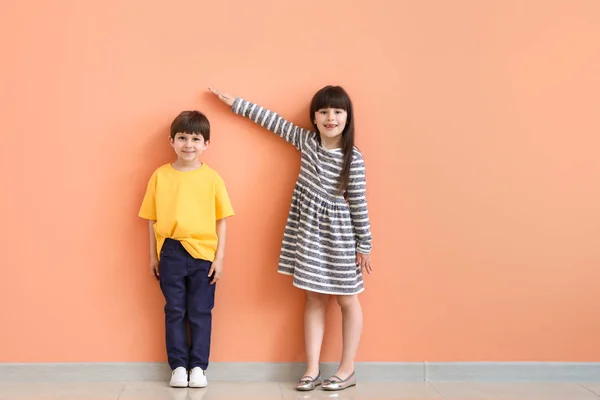 Aranyos kis gyermekek mérési magasság közelében színes fal — Stock Fotó