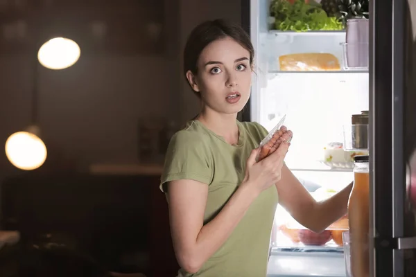 Bang vrouw gevangen in de handeling van het kiezen van smakelijke ongezond eten in de buurt van koelkast 's nachts — Stockfoto