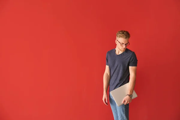 Schöner junger Mann mit Laptop auf farbigem Hintergrund — Stockfoto
