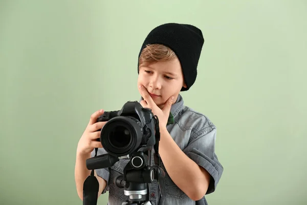 Thoughtful little photographer with professional camera on color background — Stock Photo, Image