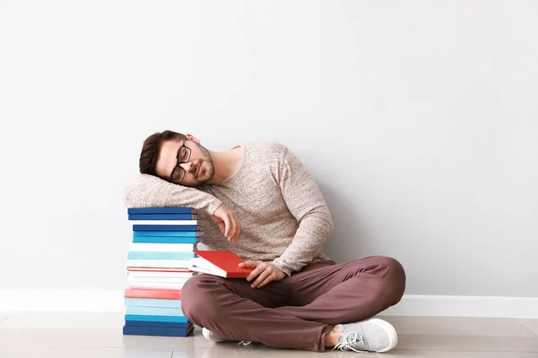 Müder junger Mann mit Büchern an Lichtwand — Stockfoto