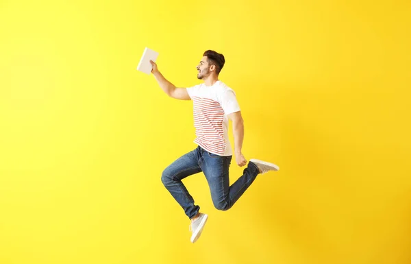 Jumping young man with book on color background — Stock Photo, Image