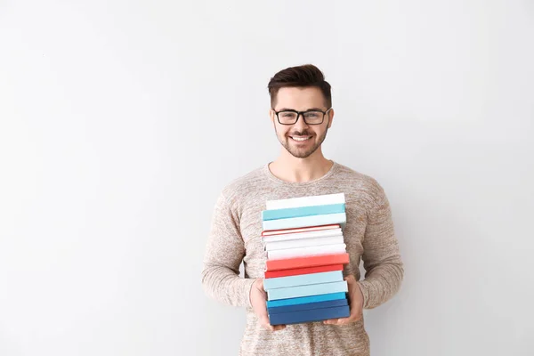 Schöner junger Mann mit Büchern auf hellem Hintergrund — Stockfoto