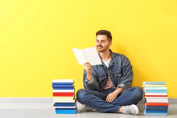 Pohledný mladý muž s knihami sedících u barevné zdi — Stock fotografie