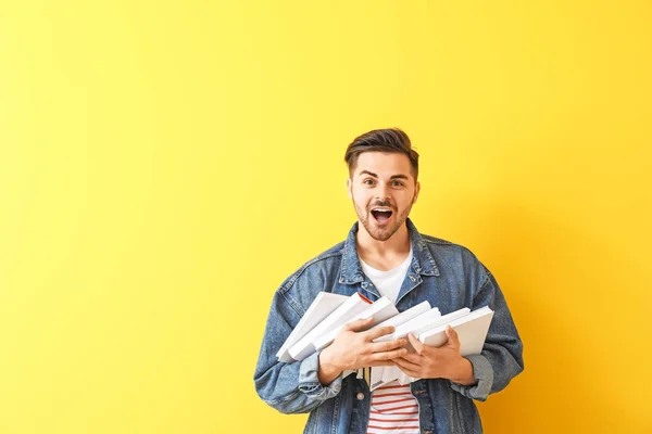 Excited young man with books on color background — Stock Photo, Image