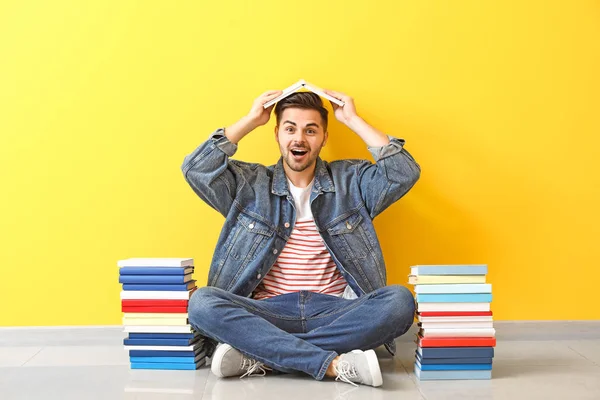 Excited young man with books sitting near color wall — Stock Photo, Image