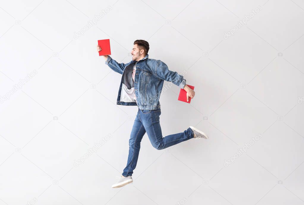 Jumping young man with books on light background