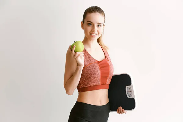 Молодая женщина с чешуей и яблоком на светлом фоне. Концепция потери веса — стоковое фото