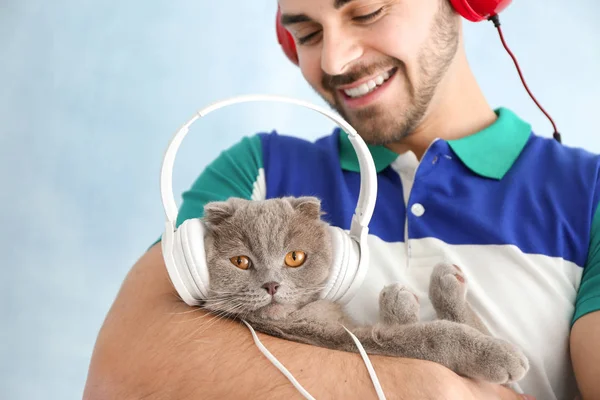 Young man and his cute funny cat with headphones on color background — Stock Photo, Image