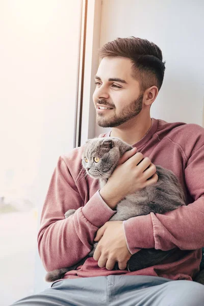 Young man with cute funny cat near window — Stock Photo, Image
