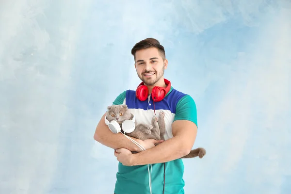 Giovane uomo e il suo simpatico gatto divertente con le cuffie su sfondo di colore — Foto Stock