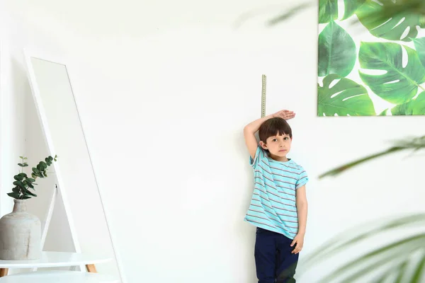 Cute little boy measuring height near wall — Stock Photo, Image