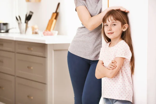 Mother measuring height of little girl near wall — Stock Photo, Image