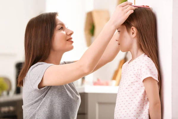 Mother measuring height of little girl near wall — Stock Photo, Image