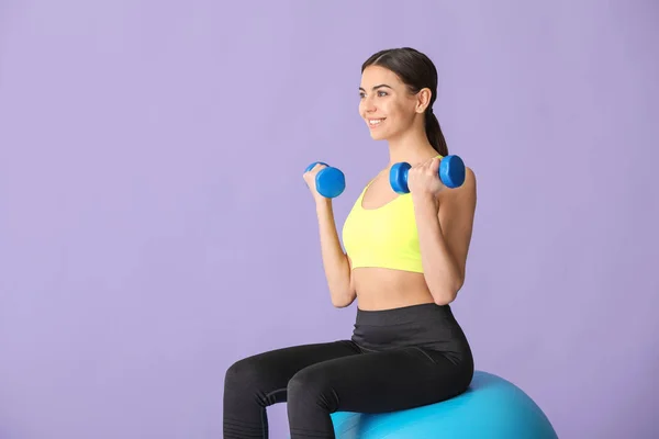 Joven mujer deportiva haciendo ejercicios con fitball sobre fondo de color —  Fotos de Stock