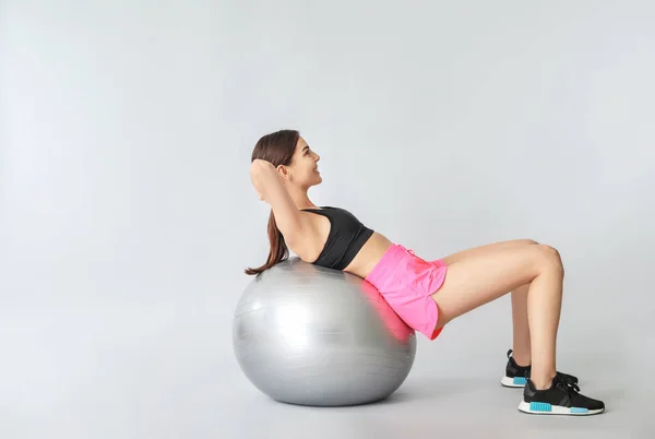 Jovem mulher esportiva fazendo exercícios com fitball no fundo cinza — Fotografia de Stock