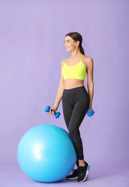 Joven mujer deportiva haciendo ejercicios con fitball sobre fondo de color —  Fotos de Stock