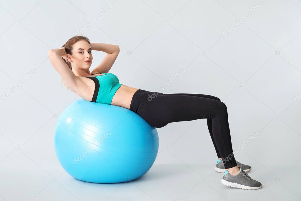 Young sporty woman doing exercises with fitball on grey background