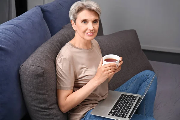 Volwassen vrouw drinken koffie tijdens het werken op laptop thuis — Stockfoto