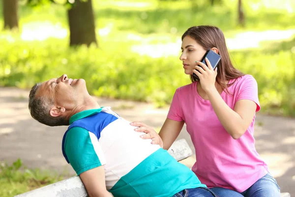 Female passer-by calling an ambulance for unconscious mature man outdoors — Stock Photo, Image