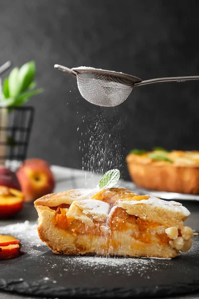 Розбризкування цукрового порошку на шматочку смачного персикового пирога — стокове фото