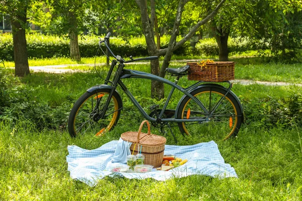 Bicycle and wicker basket with tasty food and drink for romantic picnic in park