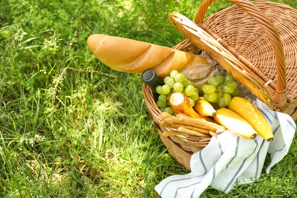 Плетений кошик зі смачною їжею та напоєм для романтичного пікніка в парку — стокове фото