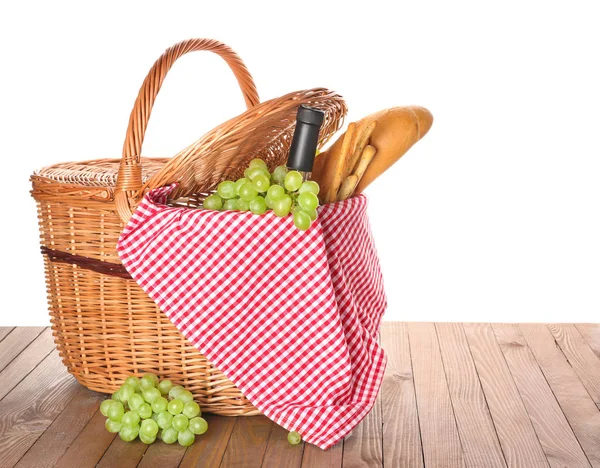 Wicker basket with tasty food and drink for picnic on wooden table against white background — Stock Photo, Image
