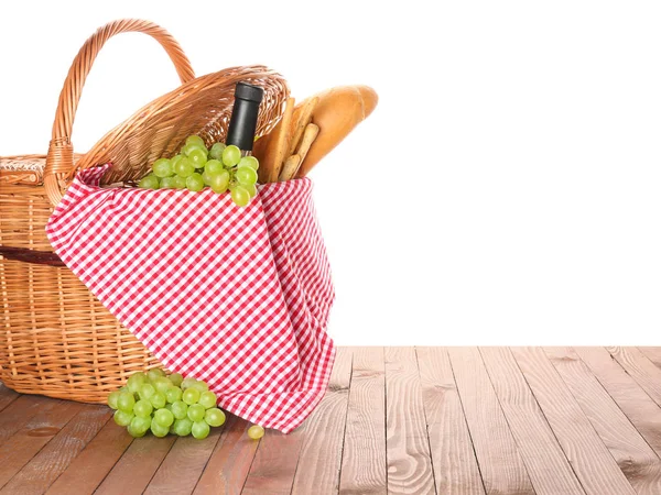 Rieten mand met lekker eten en drinken voor picknick op houten tafel tegen witte achtergrond — Stockfoto