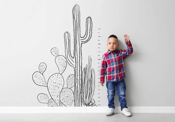 Cute Little Boy wysokość pomiaru w pobliżu światła ściany z narysowanych kaktusów — Zdjęcie stockowe